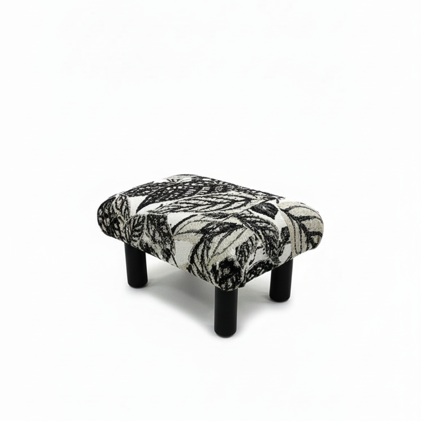 Handcrafted small footstool with black wood legs. It has a black and white leaf pattern fabric top.  It is displayed on a whitebackground. Made by Little Forest Studio