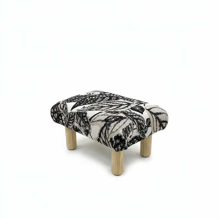 Handcrafted small footstool with natural color wood legs. It has a black and white leaf pattern fabric top.  It is displayed on a whitebackground. Made by Little Forest Studio