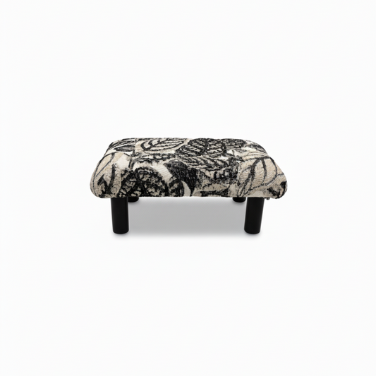 Handcrafted small footstool with black wood legs. It has a black and white leaf pattern fabric top.  It is displayed on a whitebackground. Made by Little Forest Studio