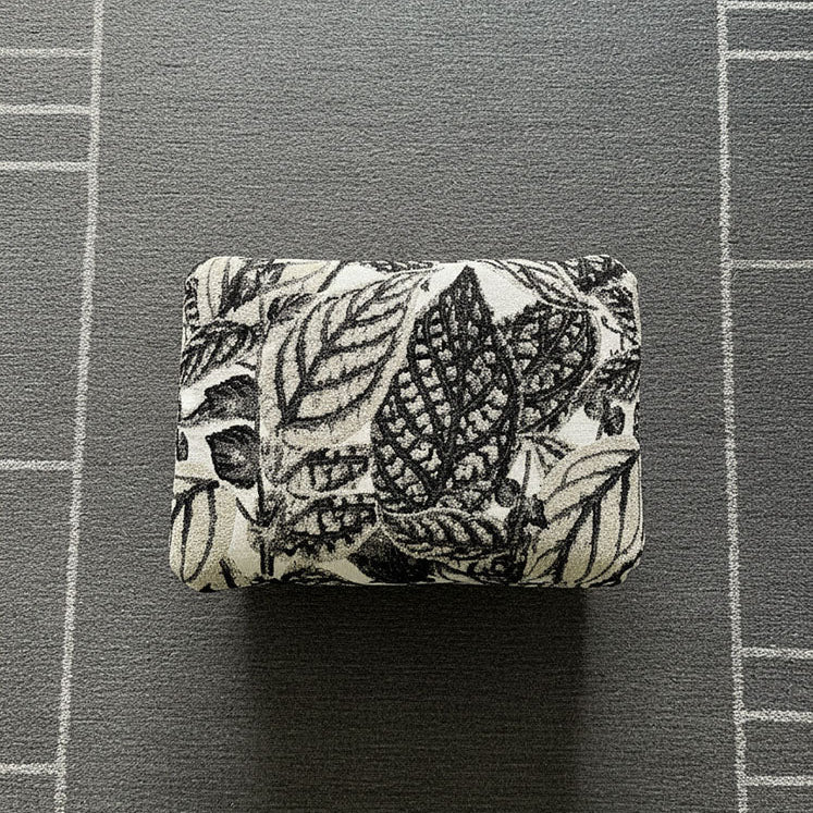 Handcrafted small footstool top. It has a black and white leaf pattern fabric top.  It is displayed on a grey rug. Made by Little Forest Studio